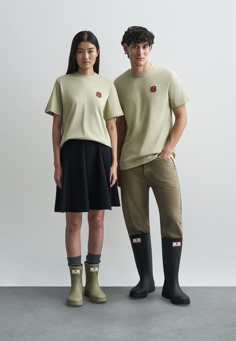 Mäkké zelené bavlnené tričká s malým vyšitým logom, tmavá sukňa, béžové kordové nohavice, zelené členkové a čierne vysoké gumové čižmy.