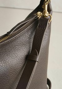 Tummanruskea nahkalaukku, jossa on teksturoitu pinta, kullanväriset metalliosat, vetoketjusuljenta ja säädettävä hihna monipuolisiin kantotapoihin.