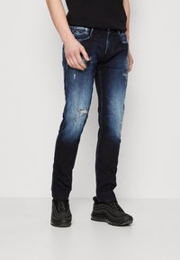 Bleka blå denimjeans med slitna detaljer, slim fit och traditionell femfickdesign. Bärs med svarta träningsskor.
