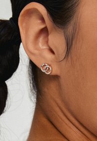 Zlatne okrugle naušnice s prepletenim uzorcima, ukrašene prozirnim rhinestones za dodatni sjaj i detalje.