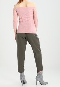 Top in pizzo leggero rosa, scollato sulle spalle, abbinato a pantaloni verdi oliva su misura e stivali a tacco grigio a quadri.