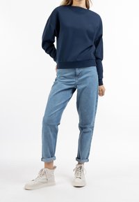 Sweat-shirt bleu marine à col rond et ourlet côtelé, associé à un jean bleu clair avec revers et des baskets montantes beiges.