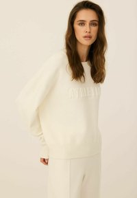 Biała, oversize'owa bluza z podniesionym napisem "ATHLETIC" z przodu, z prążkowanymi mankietami i dołem, w zestawie z pasującymi, miękkimi spodniami.