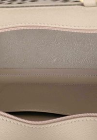 Beige handväska inuti med texturerat material. Synlig sömnad och en slät, fodrad ficka. Dragkedjestängning i öppningen.