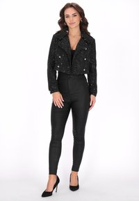 Zwarte cropped tweedjas met dubbele knopen, gecombineerd met hoge, zwarte skinny pants en zwarte puntige hakken.