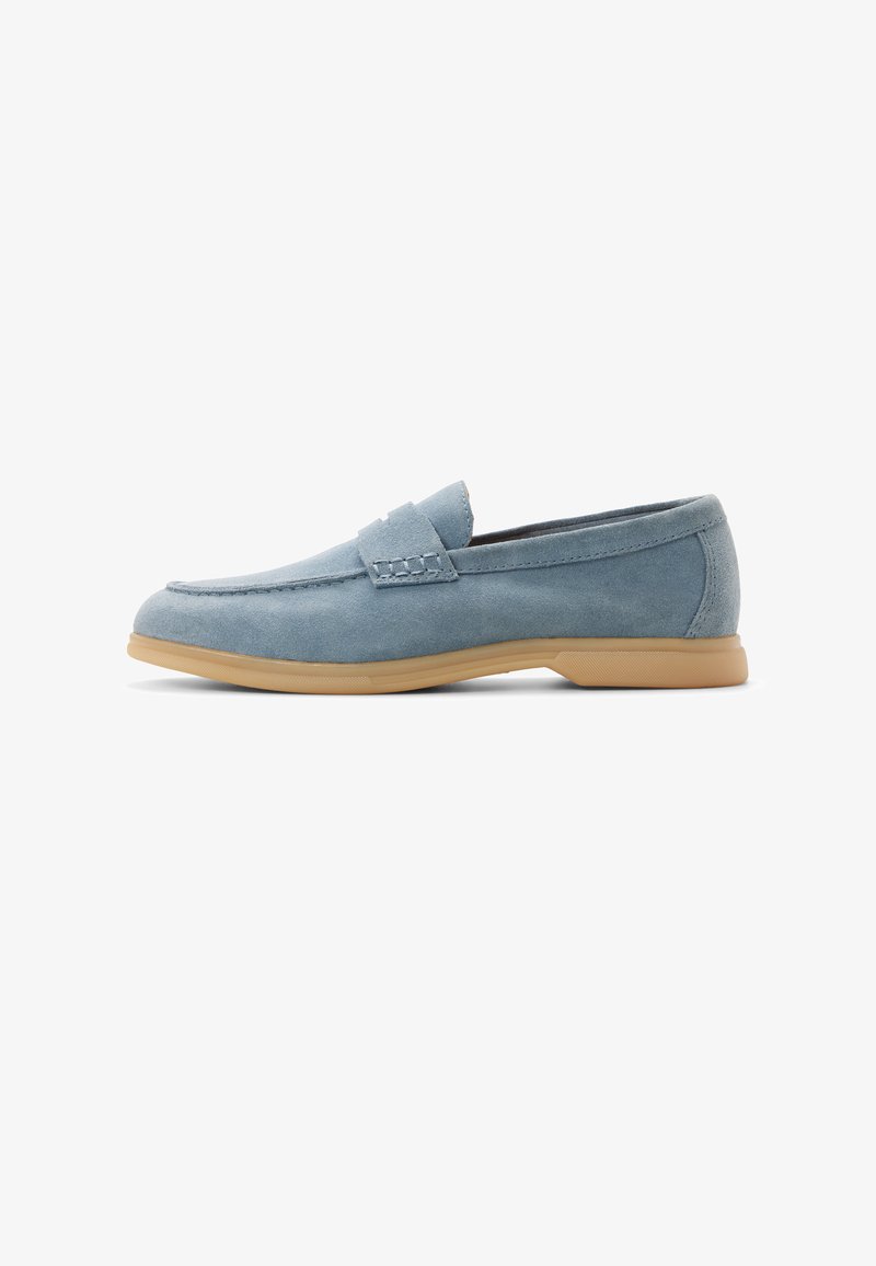 Mocasín de ante azul claro con detalles cosidos y suela de goma color caramelo, mostrado de perfil sobre un fondo blanco.