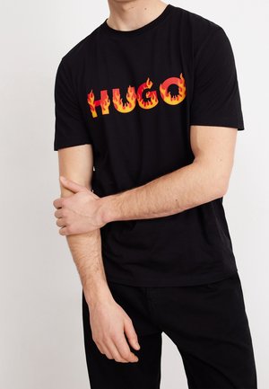 Schwarzes Baumwoll-T-Shirt mit dem Schriftzug "HUGO" in orange-roten Flammenverläufen. Kurzärmlig und mit rundem Halsausschnitt. Schlichtes, figurbetontes Design.