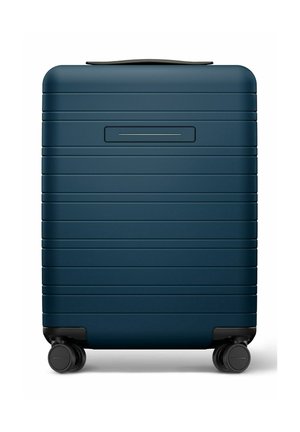 Valise rigide compacte bleu foncé avec rainures horizontales, quatre roues pivotantes noires et une poignée supérieure noire.