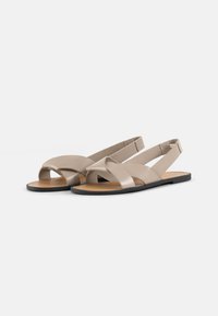Beige skinnesandaler med flatsåle, med kryssede reimer og åpen hæl. Glatt tekstur og minimalistisk design.