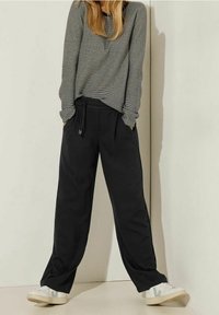 Pantalones de chándal anchos y negros con una cinturilla elástica y bolsillos laterales, combinados con una camiseta de rayas gris de manga larga y deportivas blancas.