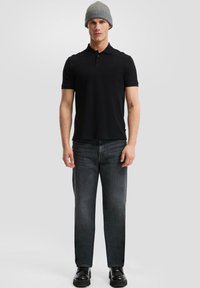 Polo shirt nera con tre bottoni, abbinata a jeans dritti grigio scuro e scarpe chunky nere. Completato con un berretto di maglia grigio.