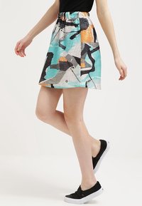 Jupe courte à motifs avec une ceinture élastique, présentant un mélange de couleurs incluant le turquoise, l'orange, le noir et le blanc dans un design abstrait.