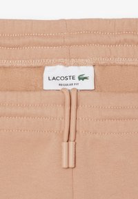 Pantaloni della tuta Lacoste regular fit in morbido tessuto pesca, con vita elasticizzata e coulisse, e etichetta con logo. Texture liscia.