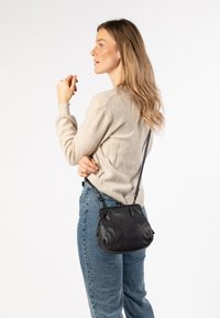 Borsa a mano in pelle nera con forma arrotondata, tracolla regolabile e finitura testurizzata, abbinata a un maglione di lana beige e jeans blu.