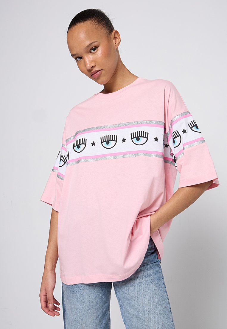 T-shirt surdimensionné rose en coton avec un design imprimé audacieux mettant en avant des yeux et des étoiles, complété par des accents argentés sur les manches.