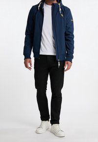 Marineblaue Zip-Jacke mit Kapuze, ausgestattet mit elastischen Bündchen und Kordelzügen, kombiniert mit einem weißen T-Shirt und schwarzen Hosen, getragen mit weißen Schuhen.