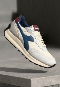 Shoe with a cream fabric upper, navy blue leather accents, burgundy heel, and textured black rubber sole. Features lace-up design.