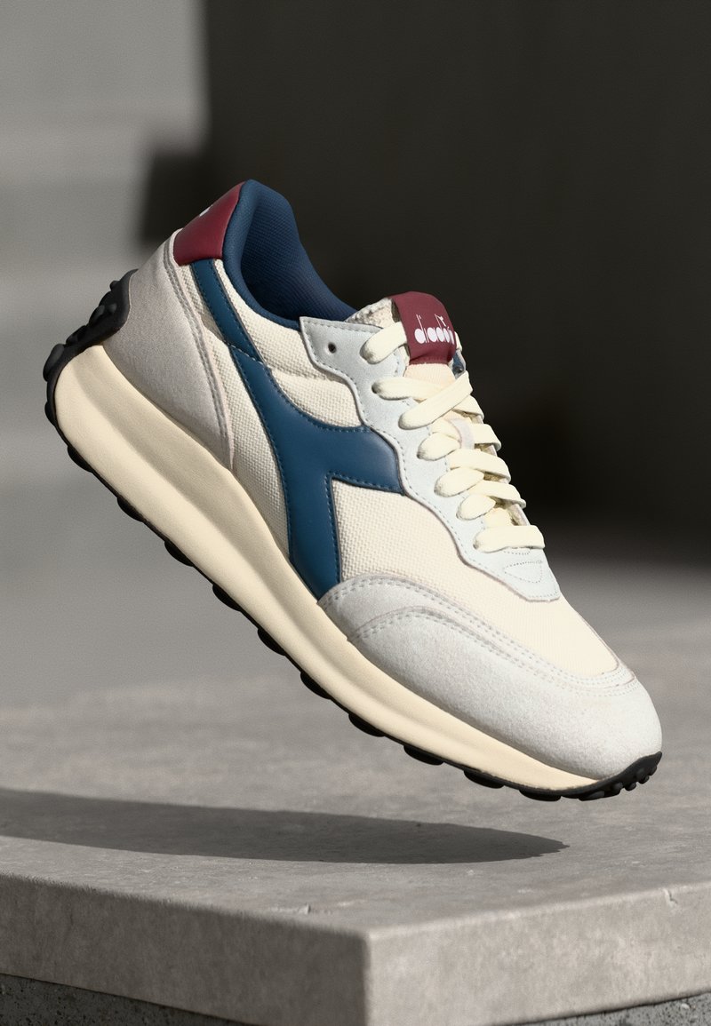 Shoe with a cream fabric upper, navy blue leather accents, burgundy heel, and textured black rubber sole. Features lace-up design.