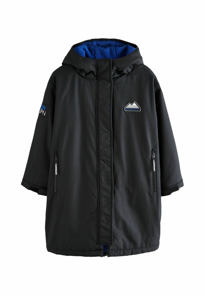 Giacca impermeabile nera con cappuccio foderato in pile blu, tasche con zip frontali e dettaglio del logo di montagna. Presenta maniche ampie e una finitura testurizzata.