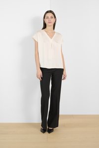 Light beige short-sleeve blouse with a V-neckline, paired with black fitted pants. Black pointed-toe heels complete the outfit. Smooth texture.