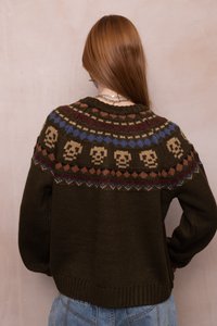 Suéter de punto en verde oliva oscuro con un cuello con diseño que presenta motivos de calaveras en colores beige, azul y óxido. Puños y dobladillo acanalados.