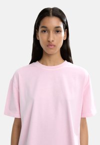 Różowa bawełniana koszulka z krótkim rękawem, okrągłym dekoltem i luźnym krojem. Gładka tekstura z widocznymi szwami wzdłuż dekoltu.