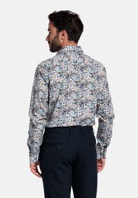 Wit overhemd met lange mouwen en een bloemendessin met blauwe, bruine en groene accenten. Getailleerde pasvorm, met knoopsluiting bij de kraag en een gladde stof.
