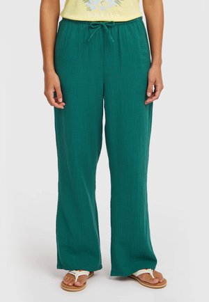 Lekkie turkusowe spodnie o szerokich nogawkach z teksturą, z paskiem ściągającym w talii. Noszone z białymi sandałami typu thong.