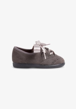 Chaussure en suède gris avec un bout arrondi, perforations décoratives et un large noeud en satin à l'avant. Semelle en caoutchouc noir.