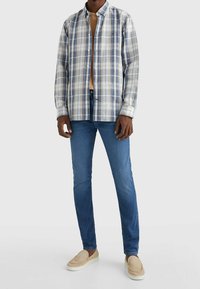 Camisa de cuadros con botones en azul, blanco y beige, combinada con vaqueros azules y zapatos beige sin cordones. La camisa tiene cuello y mangas largas.