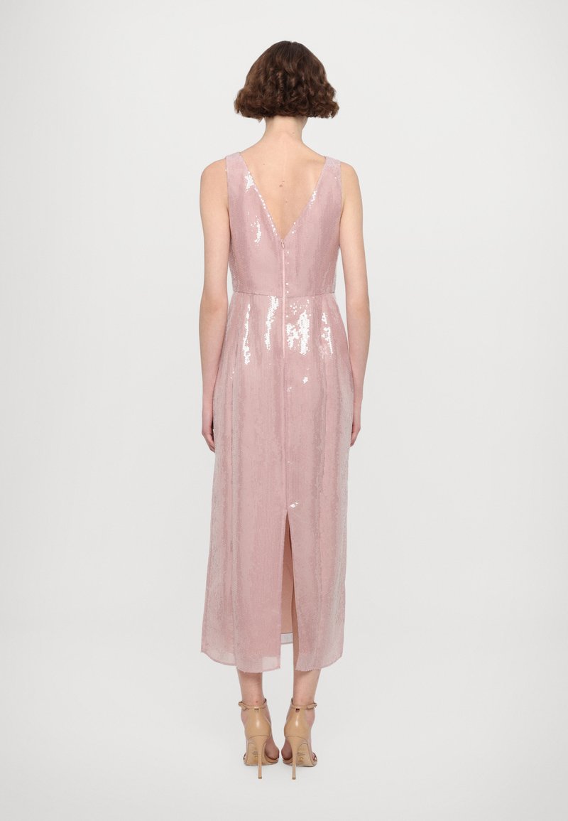 Roze paillettenjurk met een diepe V-rug, mouwloos ontwerp, knielange zoom en een split aan de achterkant. Gestyled met naakte hoge hakken.
