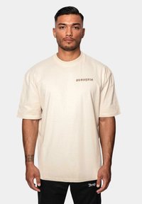 Beige oversized t-shirt lavet af bomuld, med korte ærmer og rund hals. "DROPSIZE" logoet broderet i mørkebrunt på venstre bryst.