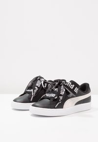 Černé kožené tenisky s bílou gumovou podrážkou, vybavené silnými černobílými branded tkaničkami a bílým bočním pruhováním.