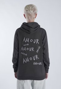 Hoodie noir avec plusieurs broderies "AMOUR" dans différentes orientations au dos. Tissu doux, capuche spacieuse et poignets côtelés.