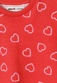 Rdeča otroška majica z vzorcem belih srčkov v obrisu in etiketom blagovne znamke Minoti, ki označuje velikost 3-4 leta, 98-104 cm.