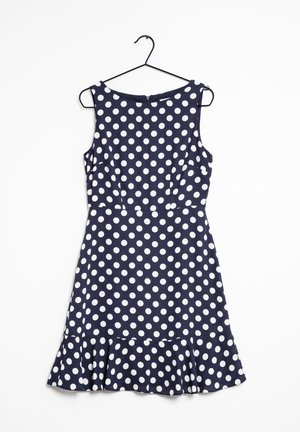 Granatowa sukienka bez rękawów w białe kropki, z dopasowaną talią i rozkloszowanym falbankowym dołem, zawieszona na czarnym wieszaku na białym tle.