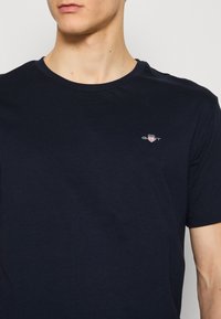 Mørkeblå bomull T-skjorte med rund hals og en liten brodert logo på brystet. Glatt tekstur med korte ermer.