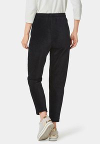 Zwarte corduroy broek met een taps toelopende pasvorm, met een elastische tailleband. Gepaard met lichtgrijze sneakers met gouden accenten.