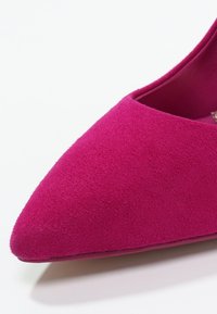 Escarpin en daim fuchsia avec un bout pointu et une texture lisse. L'intérieur est doté d'une doublure assortie, et le design est élégant et moderne.