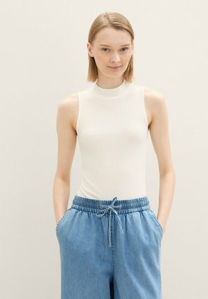 Haut sans manches blanc côtelé à col haut, associé à un pantalon en denim bleu clair, ample, avec une taille élastique et des poches.