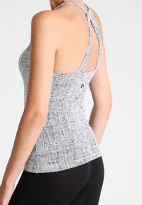 Sportovní tílko s černobílým vzorem, s designem racerback, texturovanou tkaninou a přiléhavým střihem, vhodné pro aktivní nošení.