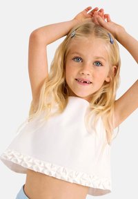 Top corto bianco con orlo arricciato testurizzato. Tessuto leggero e liscio con una vestibilità comoda. Modella in posa con le braccia sollevate.