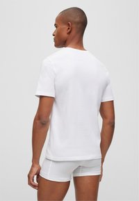 White cotton t-shirt with short sleeves, plain design, and a round neck, worn with matching white boxer shorts, viewed from the back.