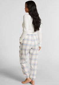 Witte lange mouwen top, gecombineerd met lichte geruite loungebroek met blauw en gele ruitjes, elastische tailleband en taps toelopende enkels.