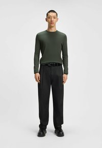 Long-sleeve, olive green top; black, relaxed-fit trousers; black belt; black sneakers; smooth texture; minimalistic design.