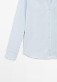 Lichtblauw overhemd met lange mouwen, rechte manchetten en zichtbare knopen op de voorkant.
