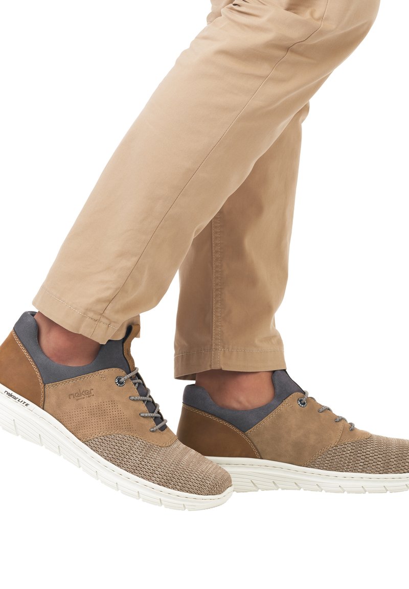 Chaussures de sport marron et grises avec une tige tissée texturée et des accents en cuir lisse. Semelle blanche avec des stries pour l'adhérence.