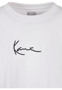 T-shirt en coton blanc avec un col rond et des manches courtes. Présente un texte brodé noir ressemblant au nom « Kani ». 