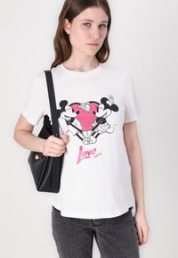 White T-shirt featuring a black graphic of Mickey and Minnie Mouse holding hands over a pink heart, with "Love" in glittery pink text.