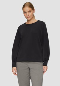 Zwarte lange mouwen sweatshirt met een ronde hals, voorzien van losse mouwen en een geribbelde zoom, gecombineerd met lichtgrijze broeken.